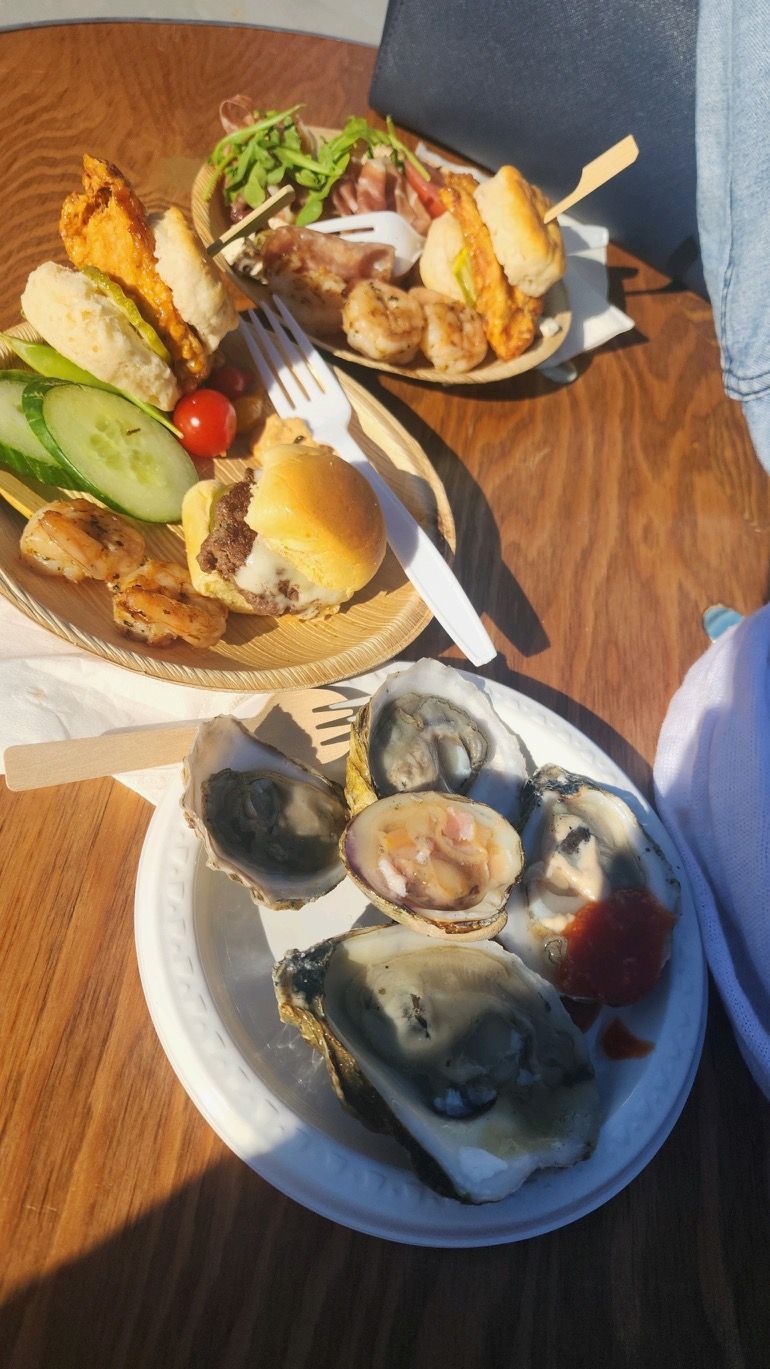 Two plates of seafood tacos and oysters on a wooden table with lemon wedges and a fork