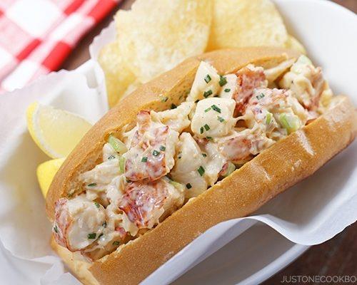 A lobster roll with chips and a slice of lemon