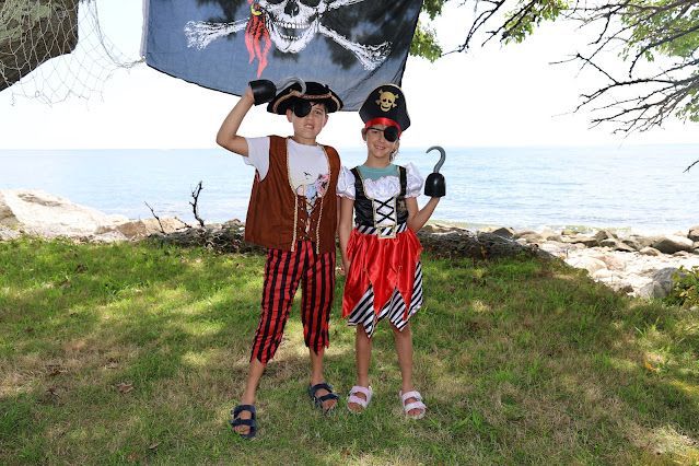Two children dressed in pirate costumes are standing in front of a pirate flag.