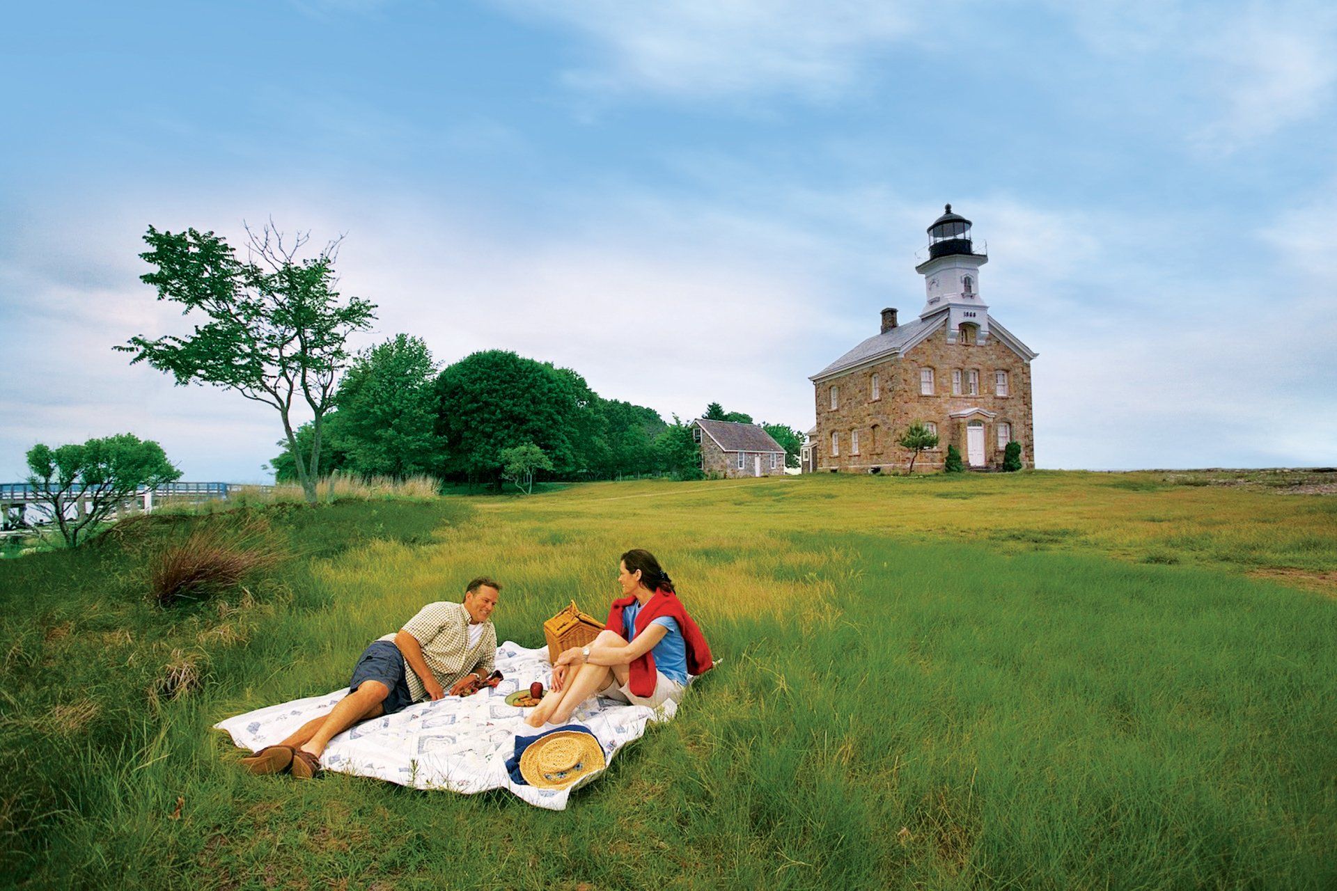 A man and woman are having a picnic in a field with a lighthouse in the background