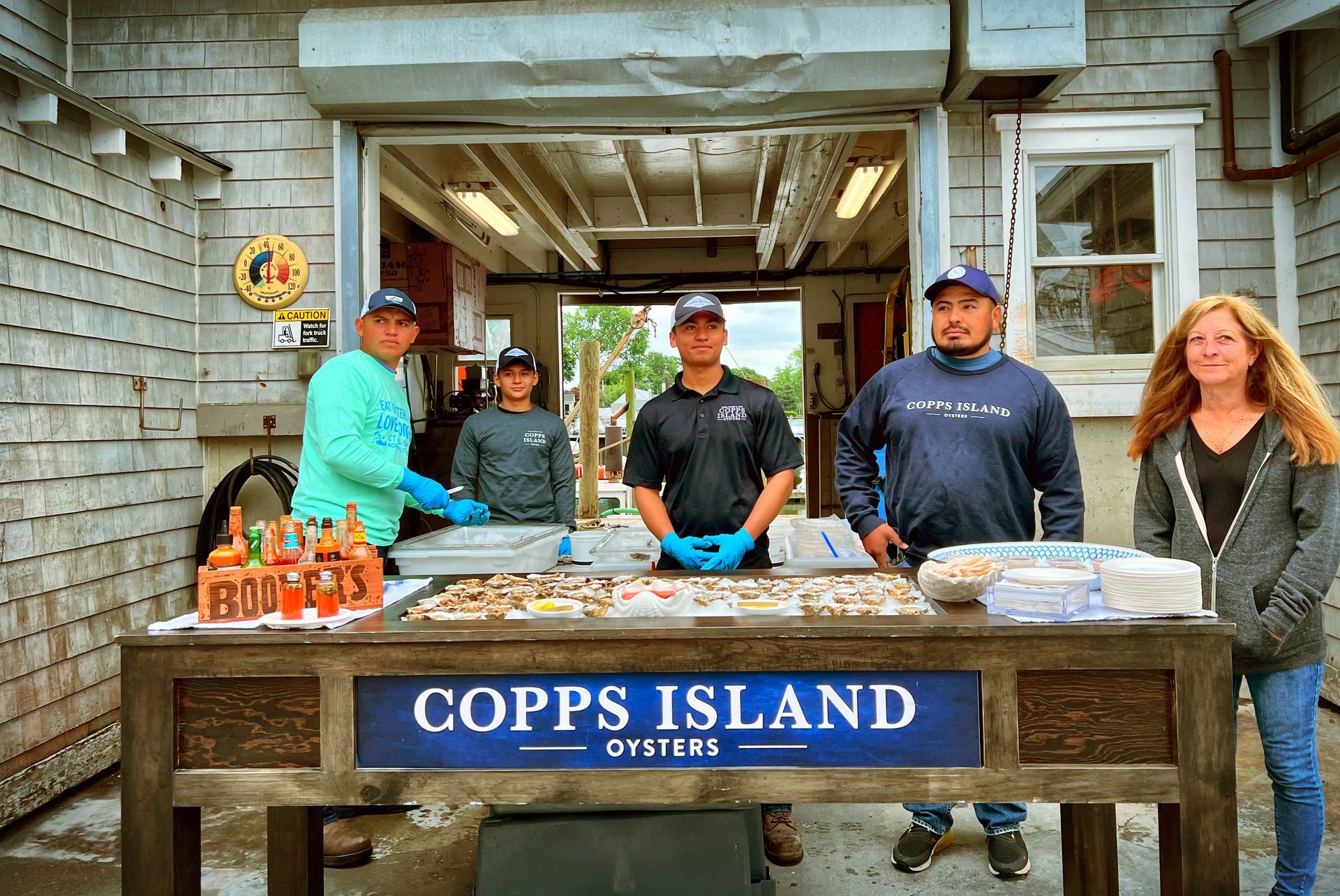 People behind a Copps Island oyster stand with trays of seafood and a blue sign.