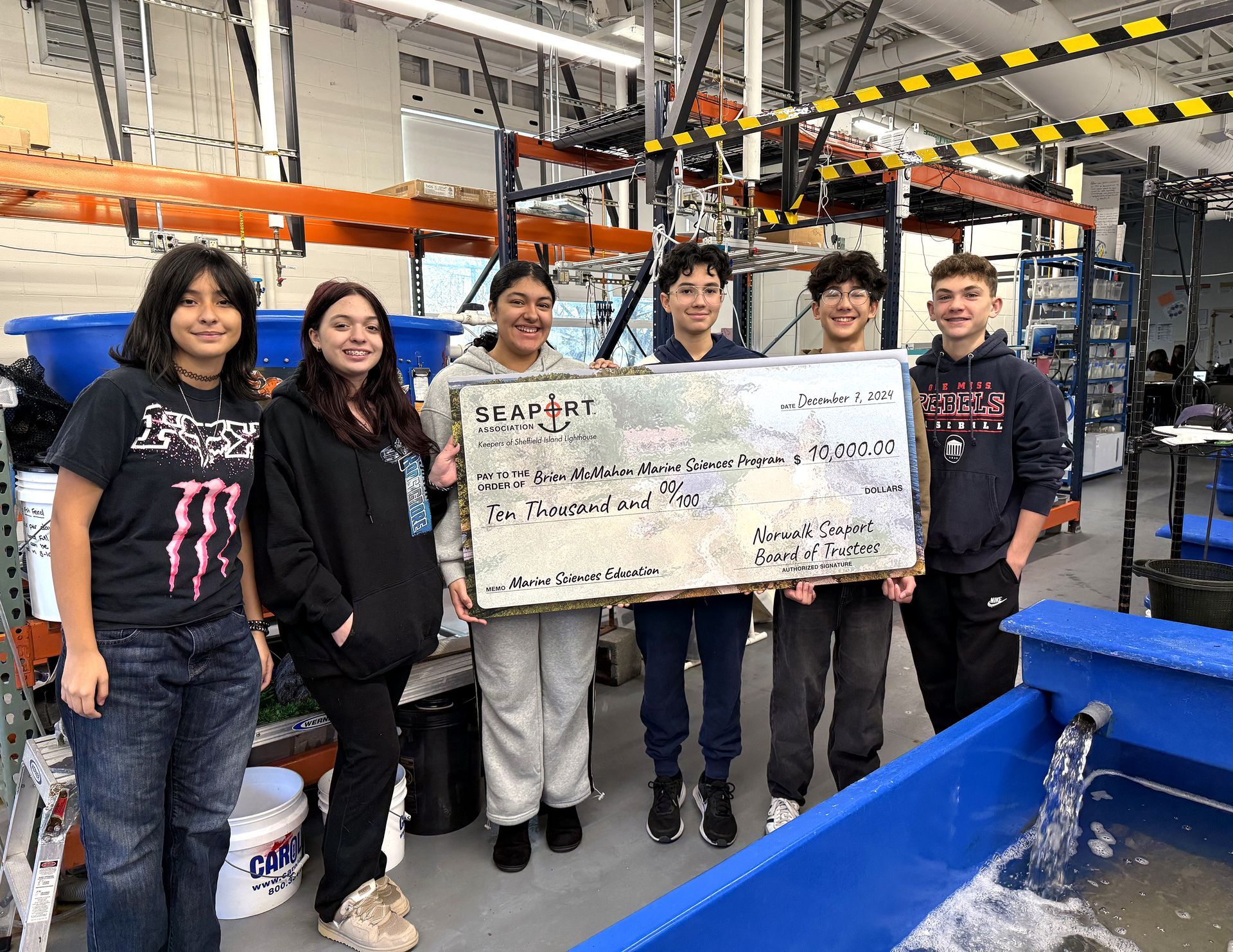 A group of young people are standing in a room holding a large check.