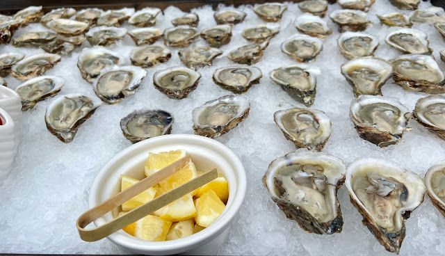 Fresh oysters on ice with a bowl of lemon wedges and tongs in the foreground