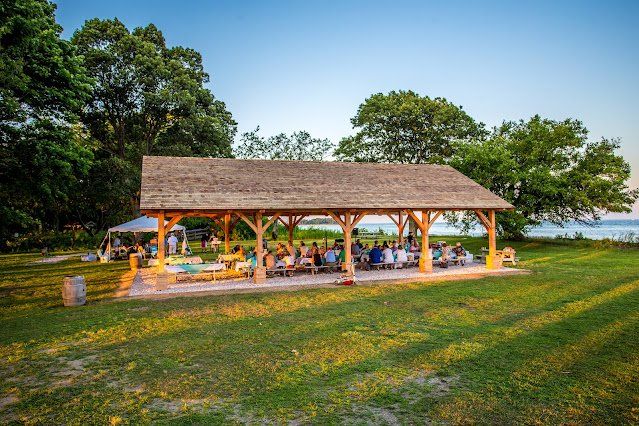 A group of people are sitting under a wooden pavilion in a park.