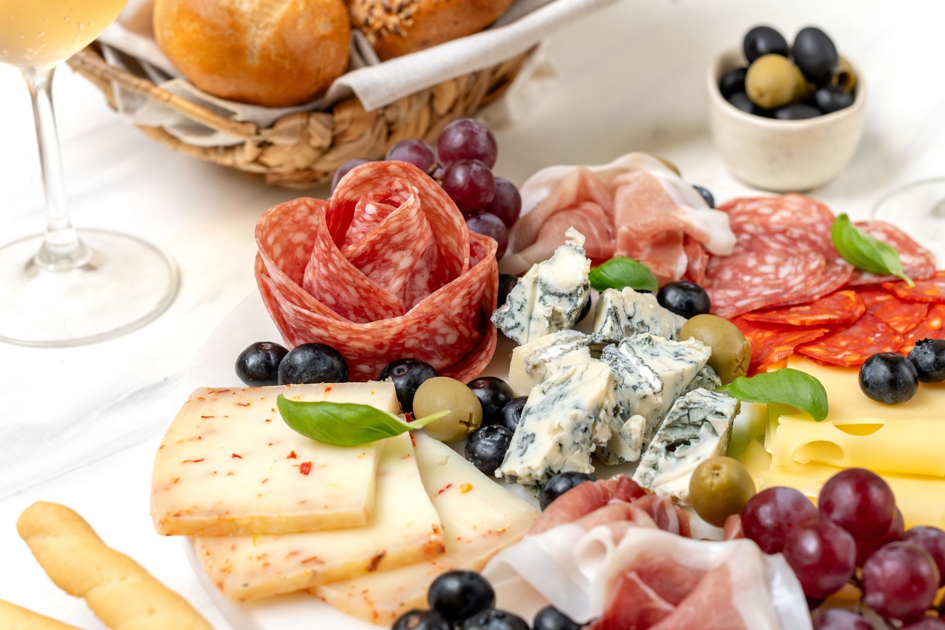 Charcuterie board with salami rose, cheeses, meats, grapes, olives, bread and wine.