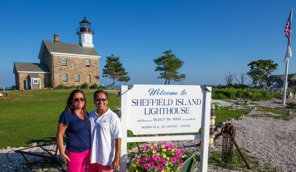 Two people are standing in front of a sign that says welcome to sheffield island lighthouse.