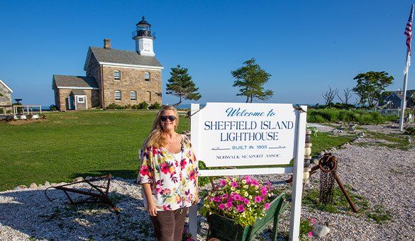 A woman is standing in front of a sign that says sheffield island lighthouse.