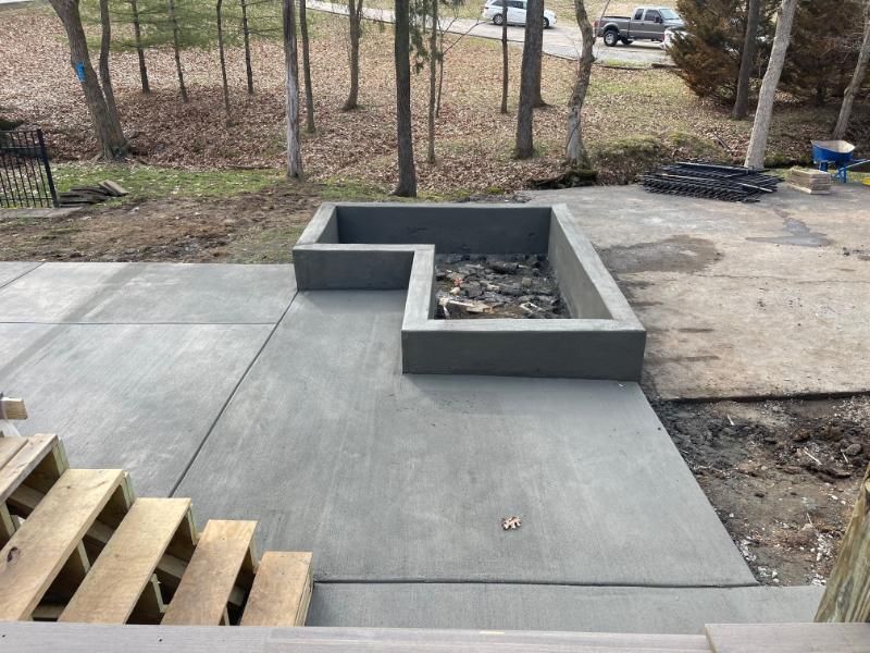 Concrete patio with a raised rectangular fire pit at a wooded backyard site
