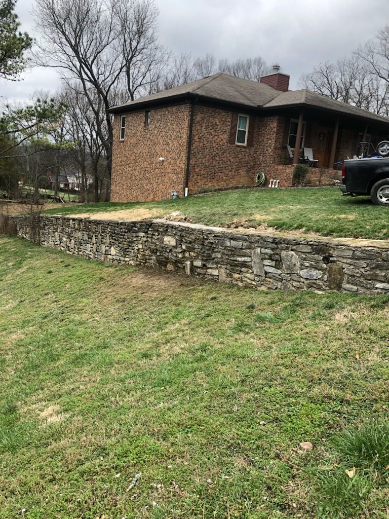 Brick house on a grassy slope with a stone retaining wall and cloudy sky