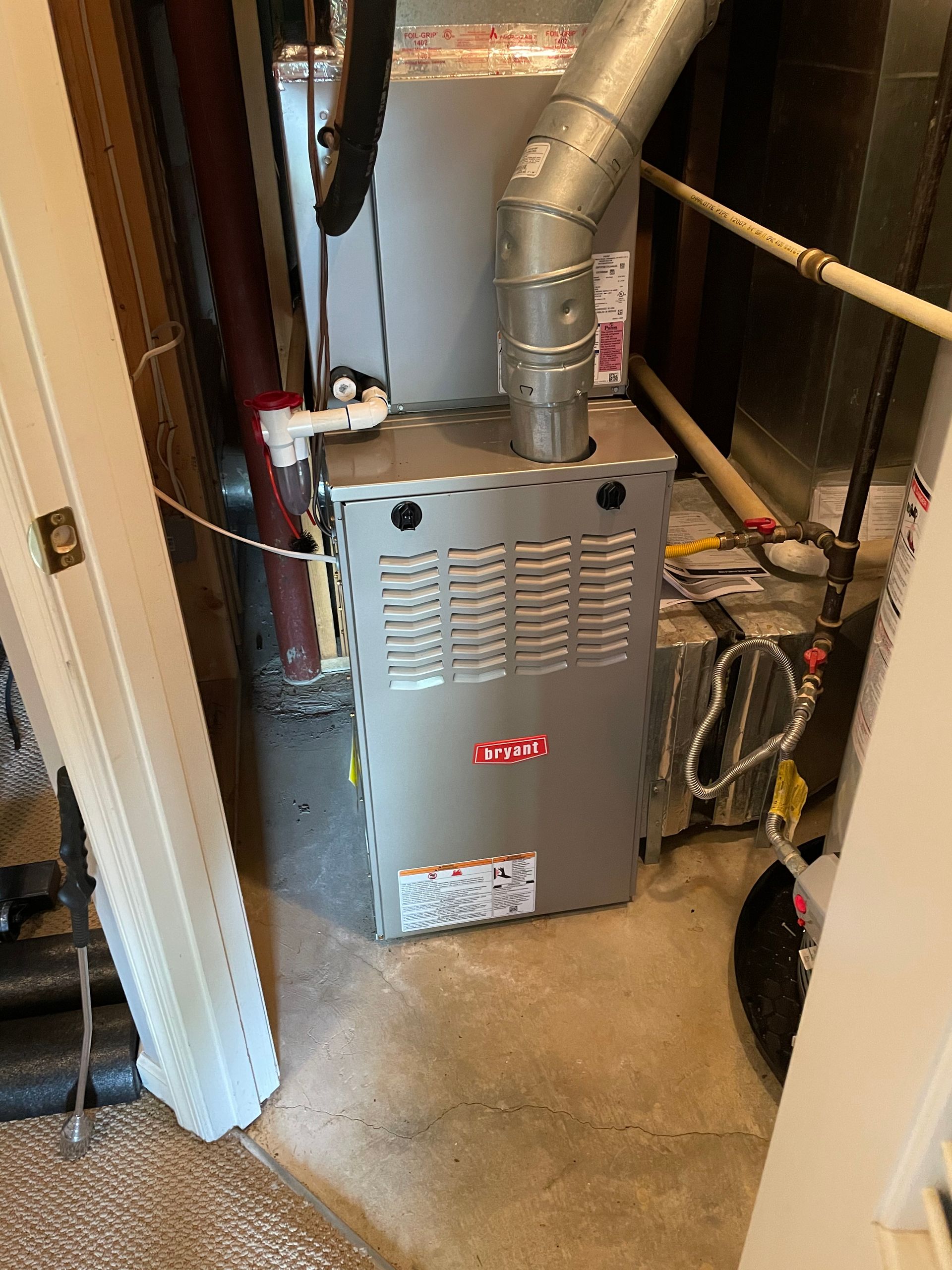 A furnace is sitting in a corner of a room next to a door.