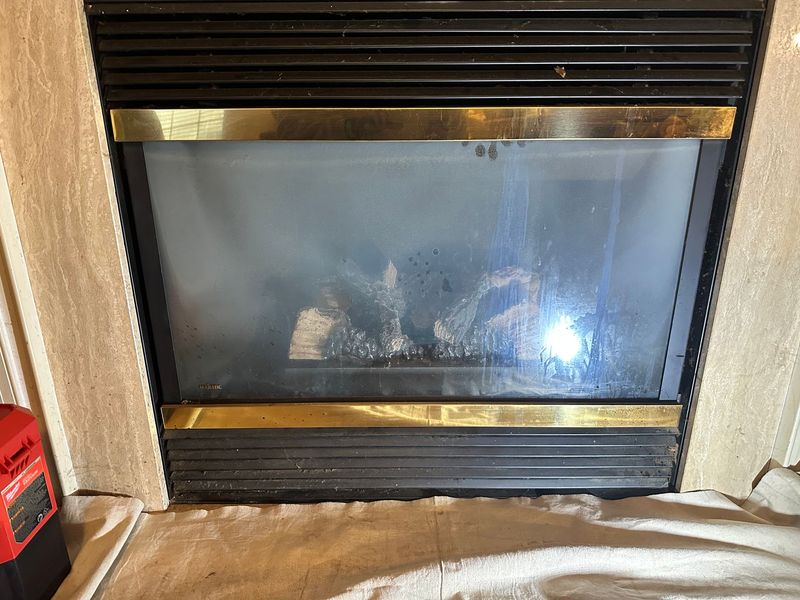 A fireplace with a glass door and a brass trim.