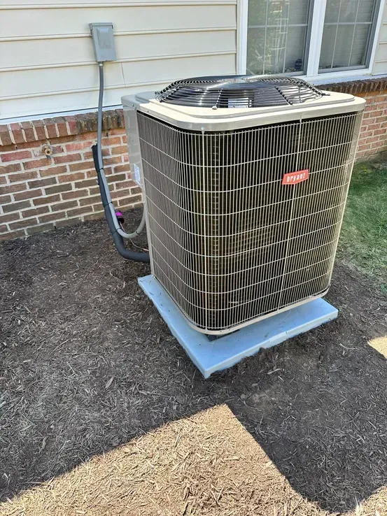 A large air conditioner is sitting outside of a brick house.