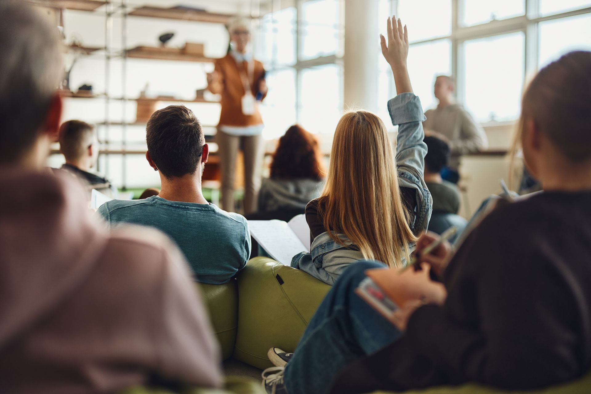 A group of people are sitting in a classroom raising their hands to answer a question. A group of people are sitting in a classroom raising their hands to answer a question.