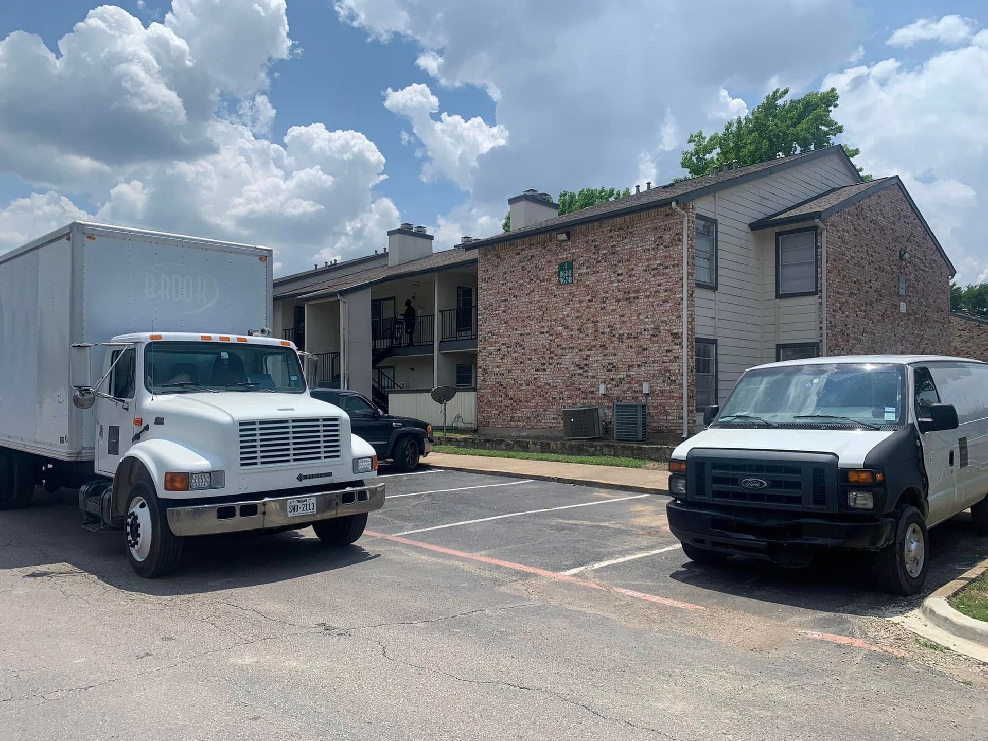 Two white delivery trucks parked in a lot beside a brick building under a cloudy sky