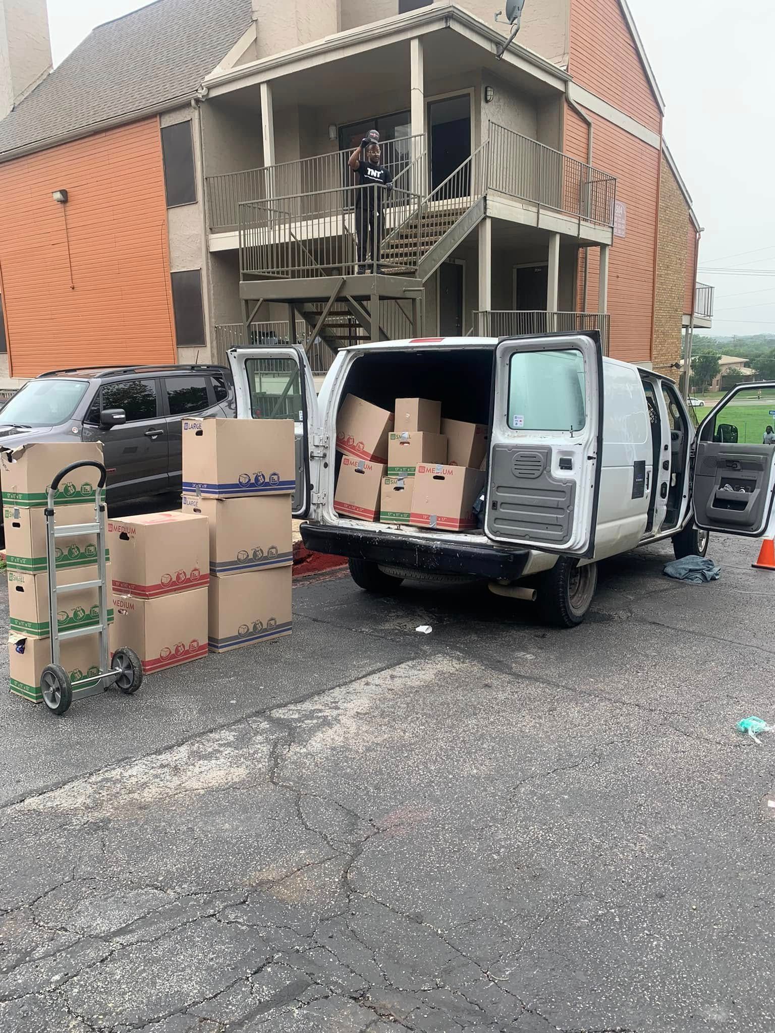 Delivery vans unloading cardboard boxes outside a damaged building with broken balcony railings.