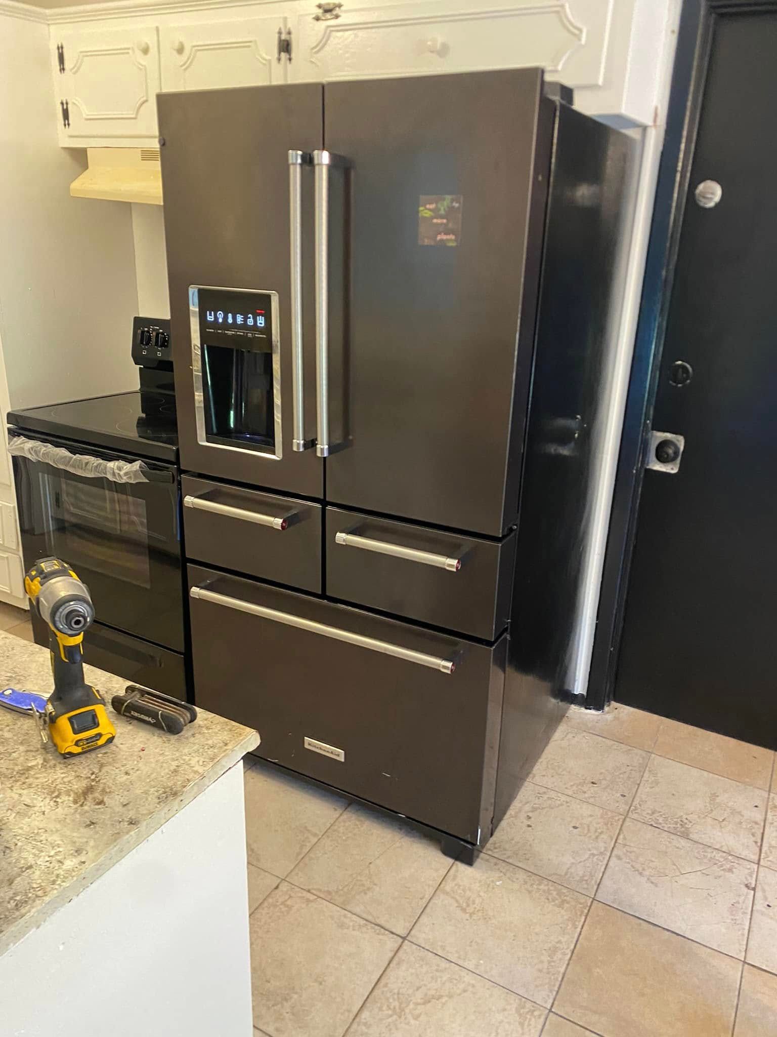 Dark stainless steel French-door refrigerator with water dispenser in a kitchen beside a black oven.