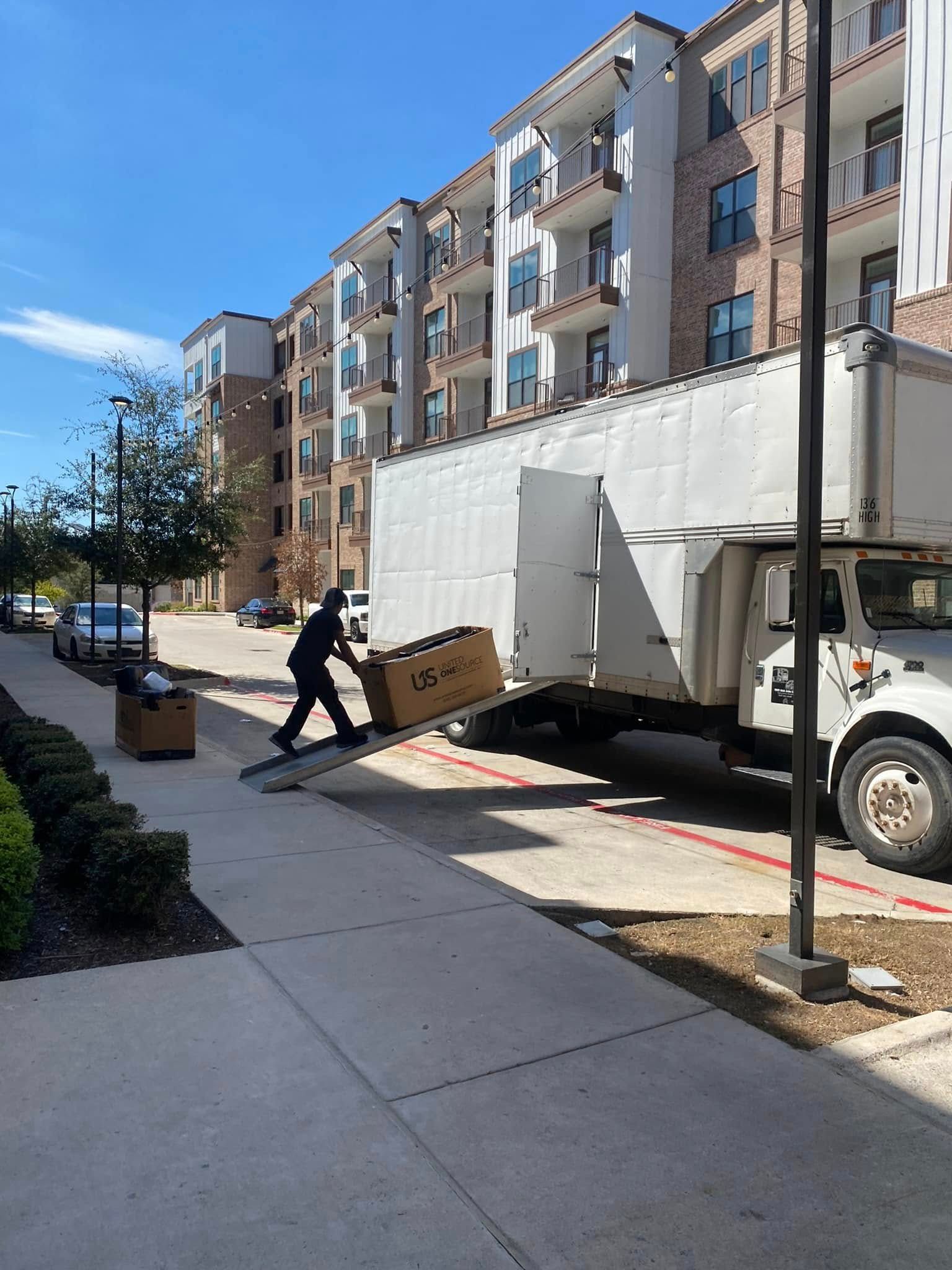 Delivery worker unloading boxes beside a white box truck on a sunny apartment street