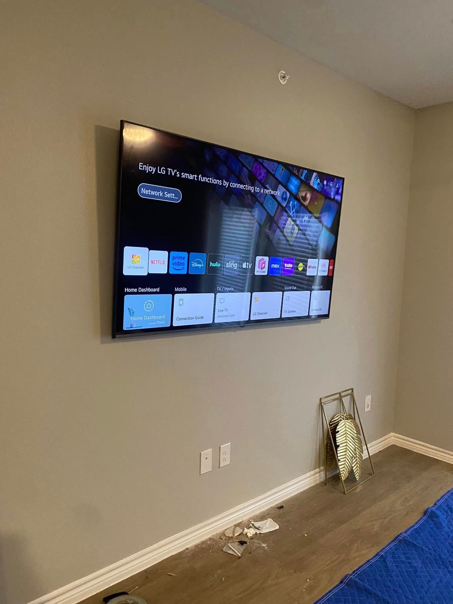 Wall-mounted TV in a beige room with blue carpet and a decorative wreath on the floor.