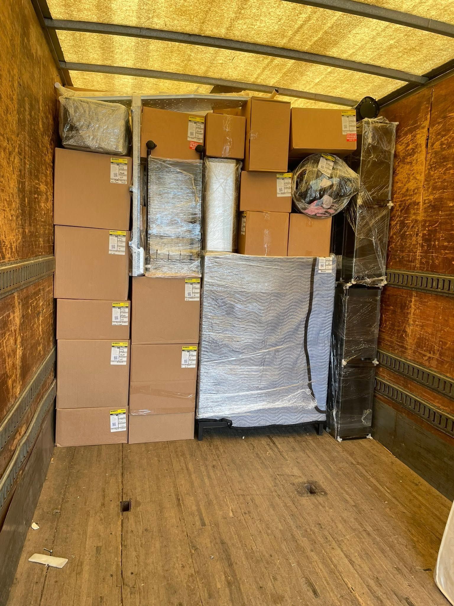 Packed moving truck with stacked cardboard boxes and wrapped furniture inside.