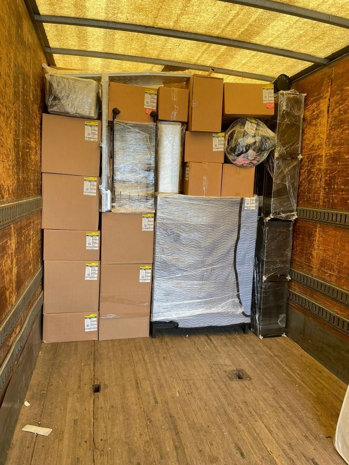 Packed cardboard boxes and wrapped items stacked inside the back of a moving truck.