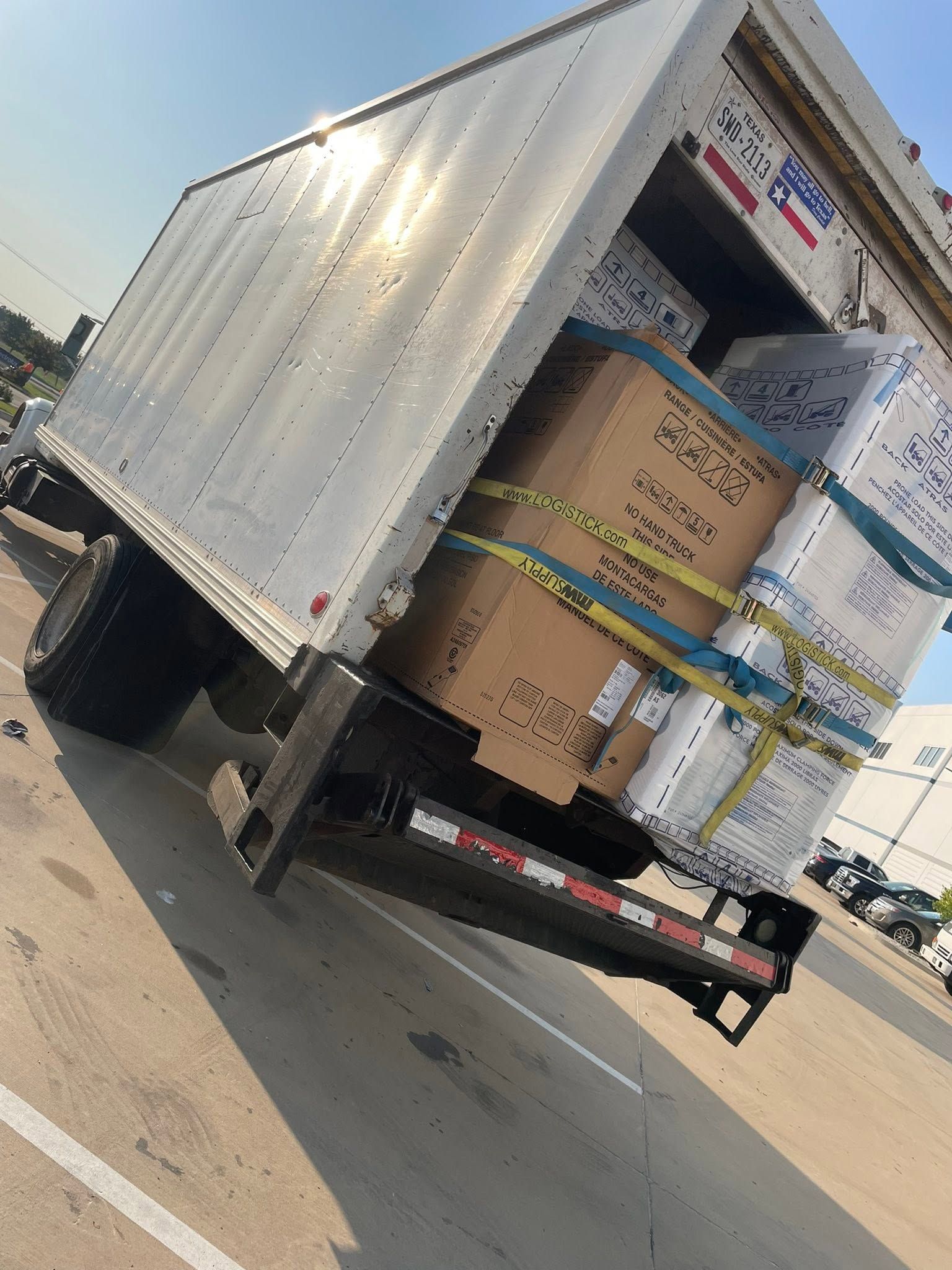 Tilted white box truck carrying stacked cardboard boxes on a highway