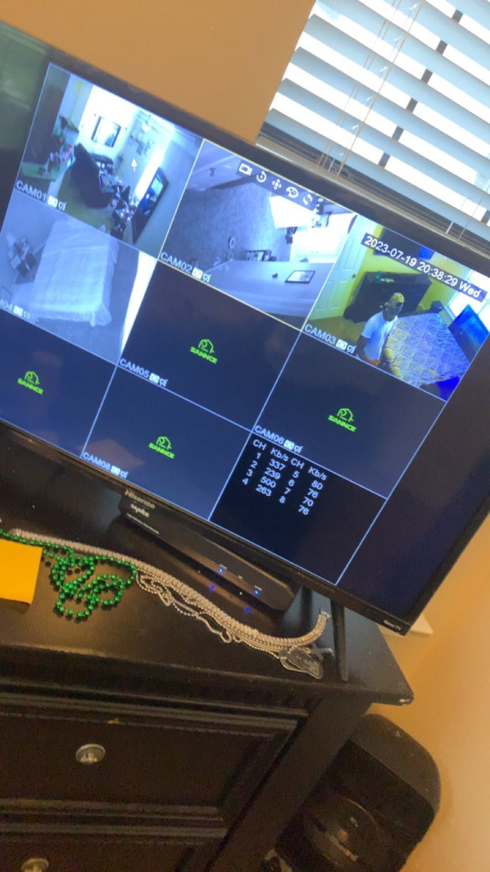 Wall-mounted CCTV monitor showing multiple security camera views in a room with a dresser below