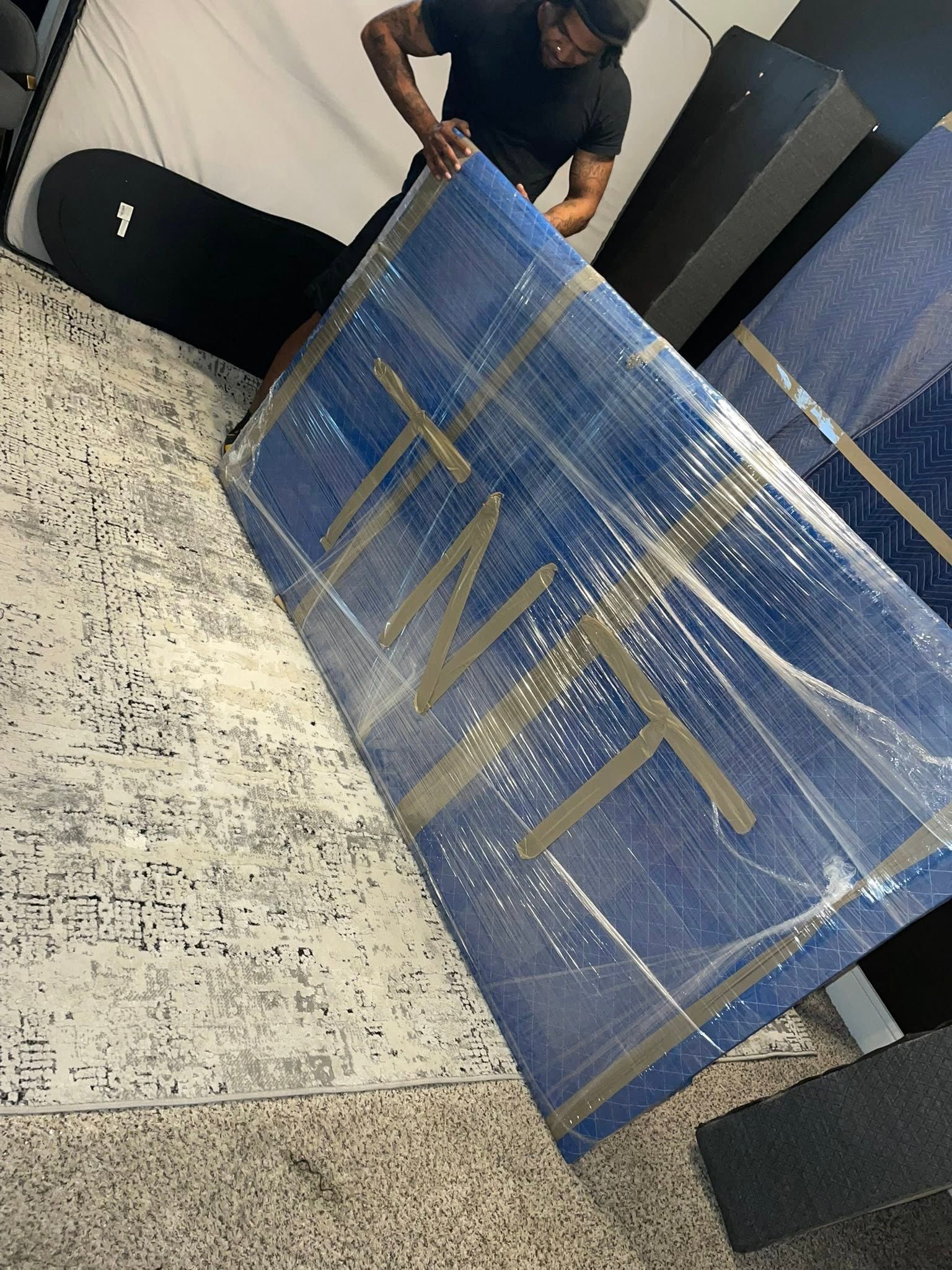 Person wrapping a blue sign with gold letters in clear plastic wrap indoors.