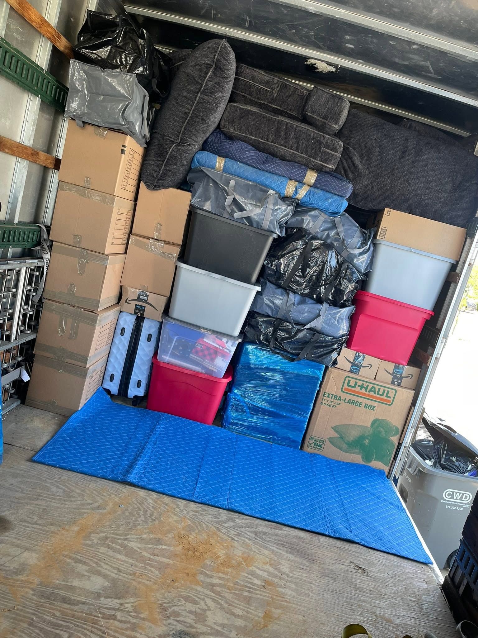 Packed moving truck with stacked boxes, plastic bins, and blue floor padding inside.