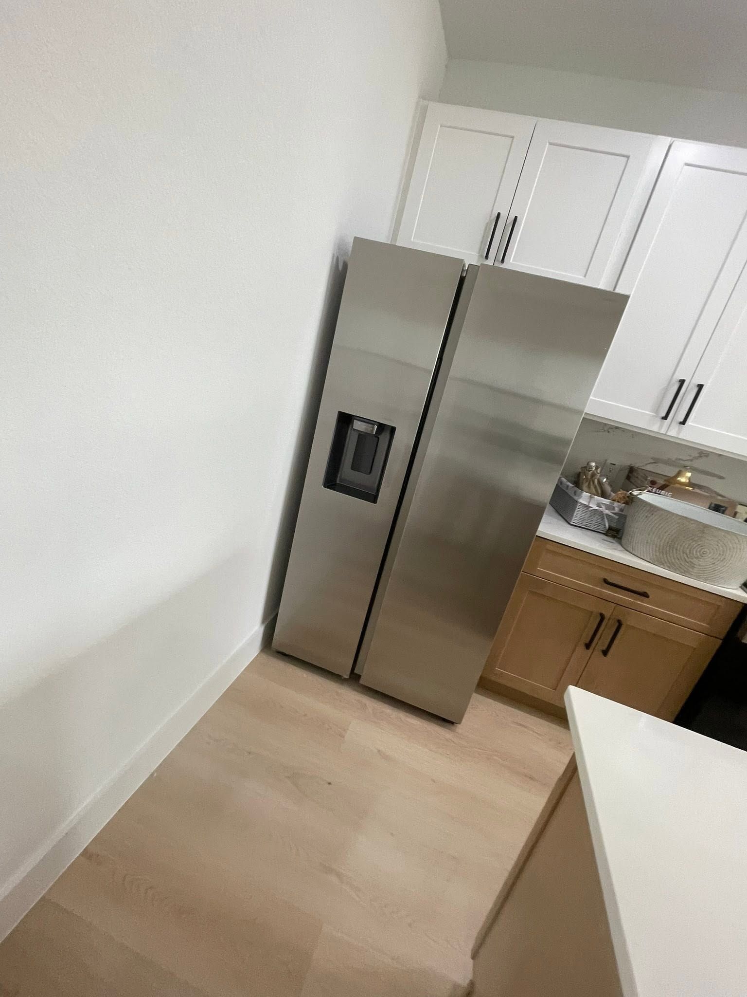 Modern kitchen with stainless steel refrigerator, white cabinets, wood floors, and sink area
