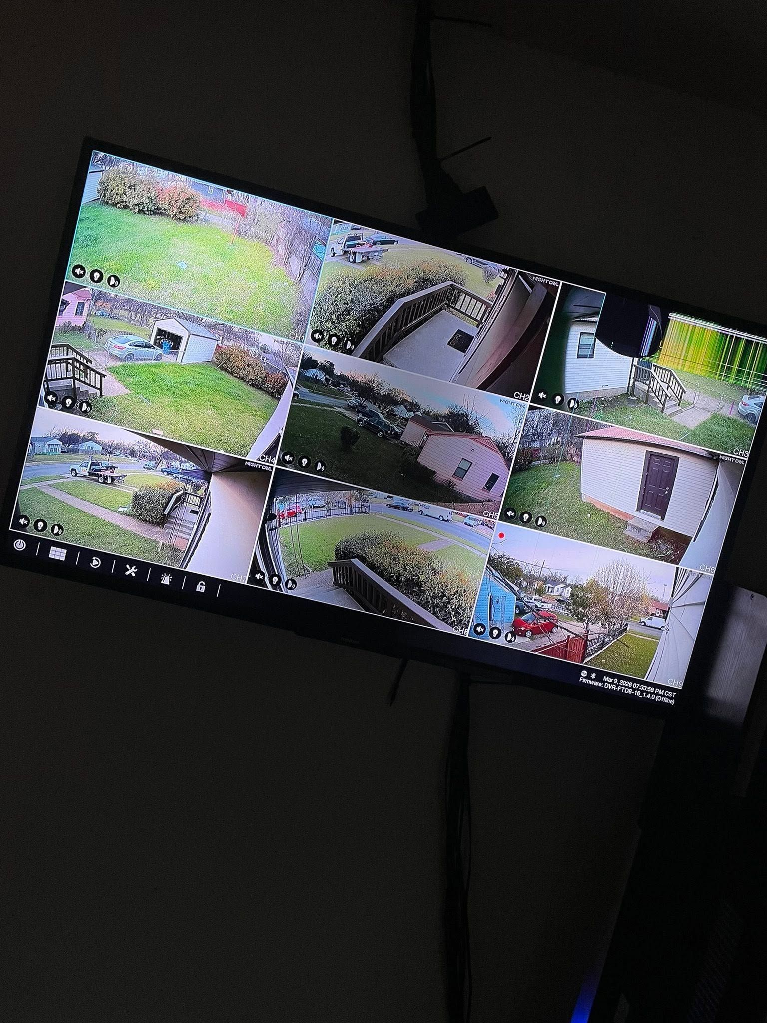 Tilted wall-mounted TV showing a multi-camera security monitor feed at night