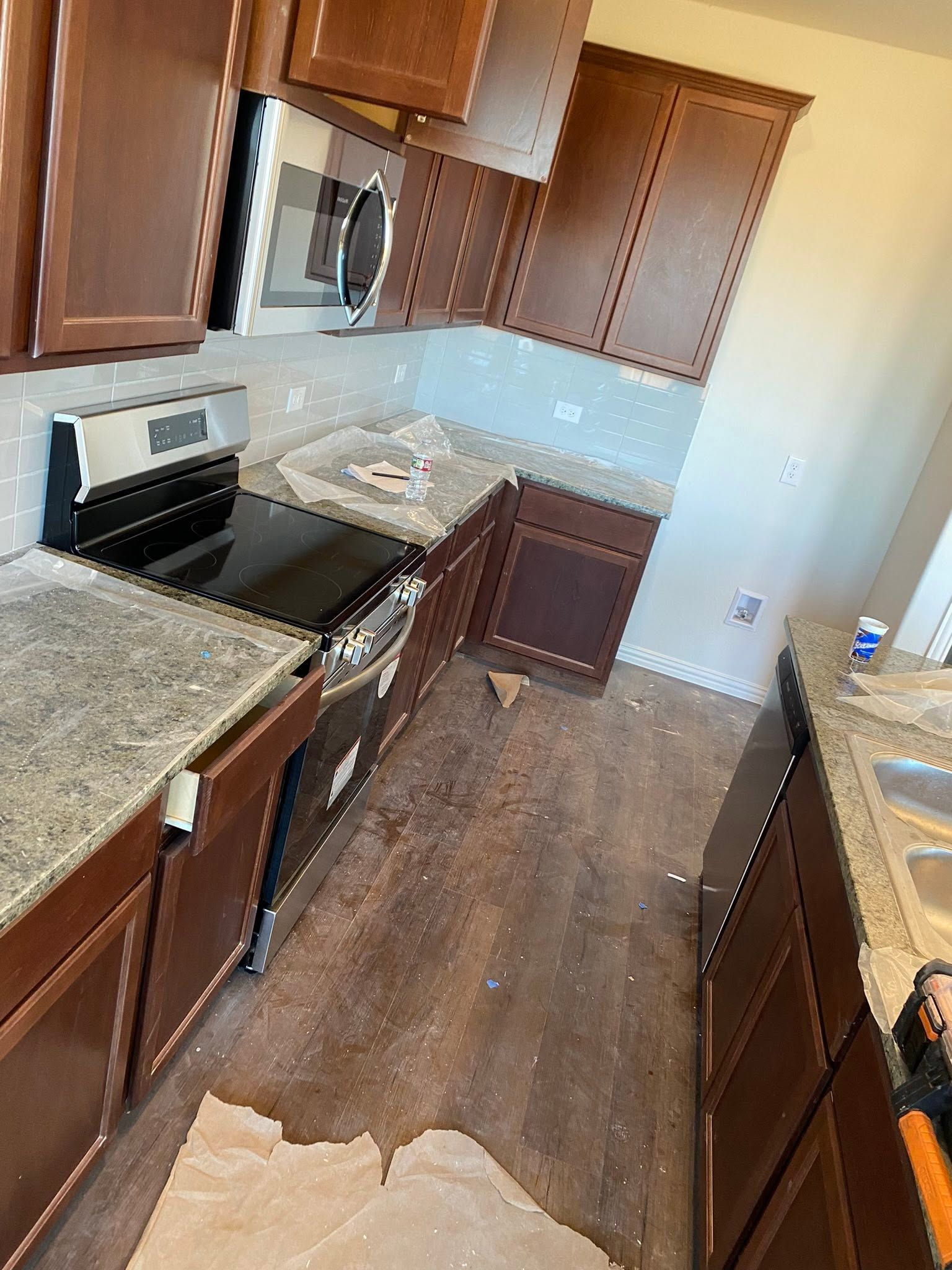 Damaged kitchen with muddy water spill on the floor, dark wood cabinets, and granite countertops.