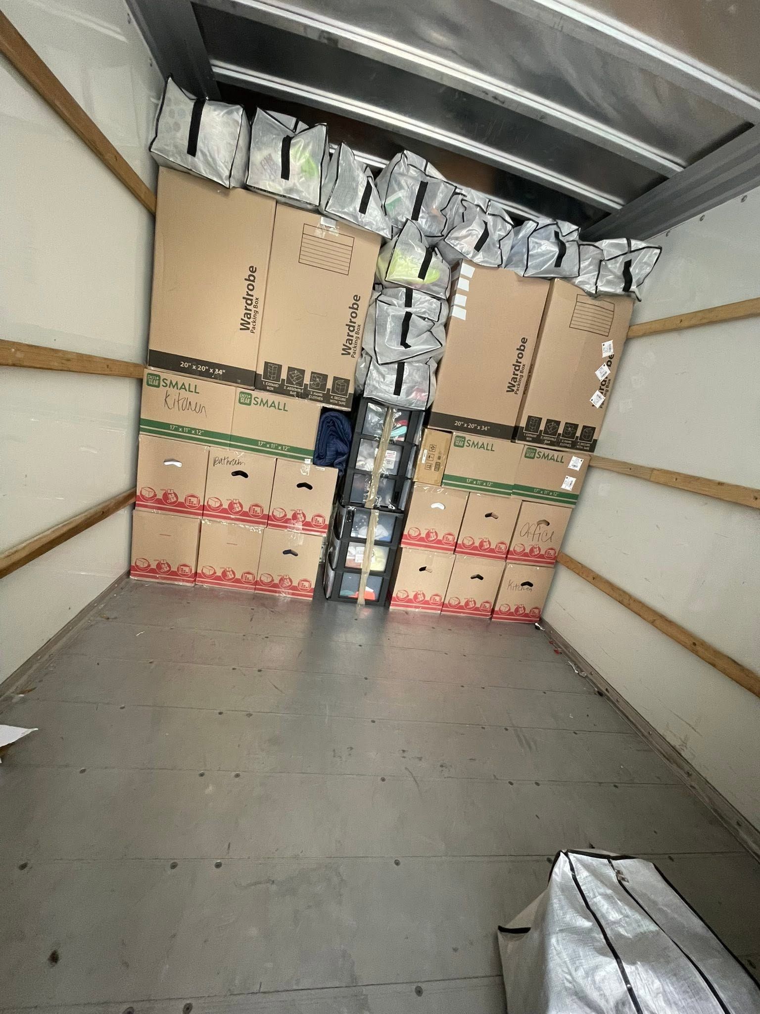 Inside a cargo truck, stacked cardboard boxes and wrapped packages block the back wall.