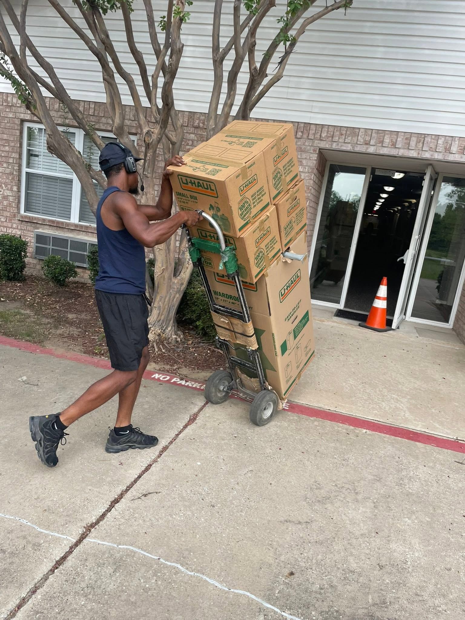 Person pushing a large cardboard box on a dolly outside a building entrance