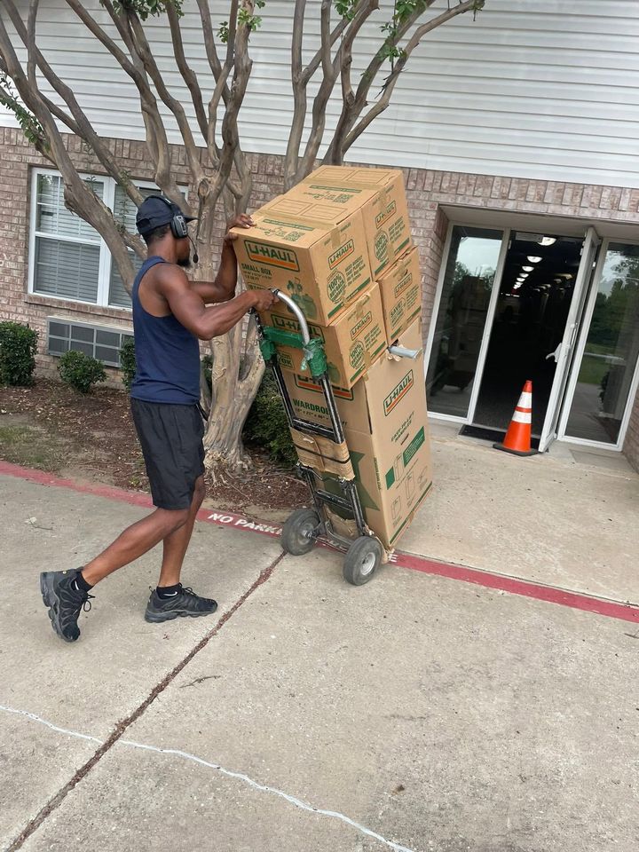 Person pushing a large cardboard box on a hand truck outside a building entrance