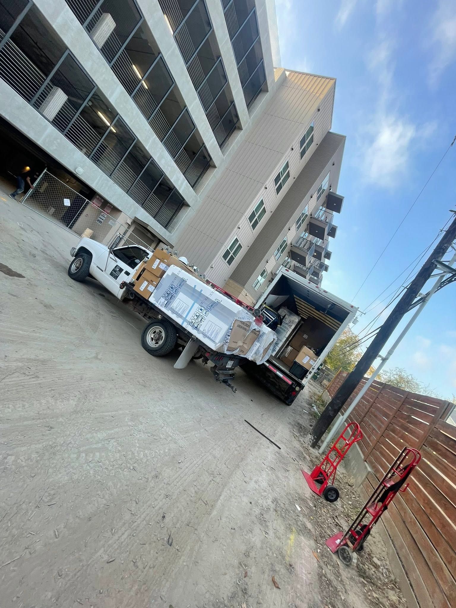 White utility truck unloading at a tilted city construction site beside a building and crane.