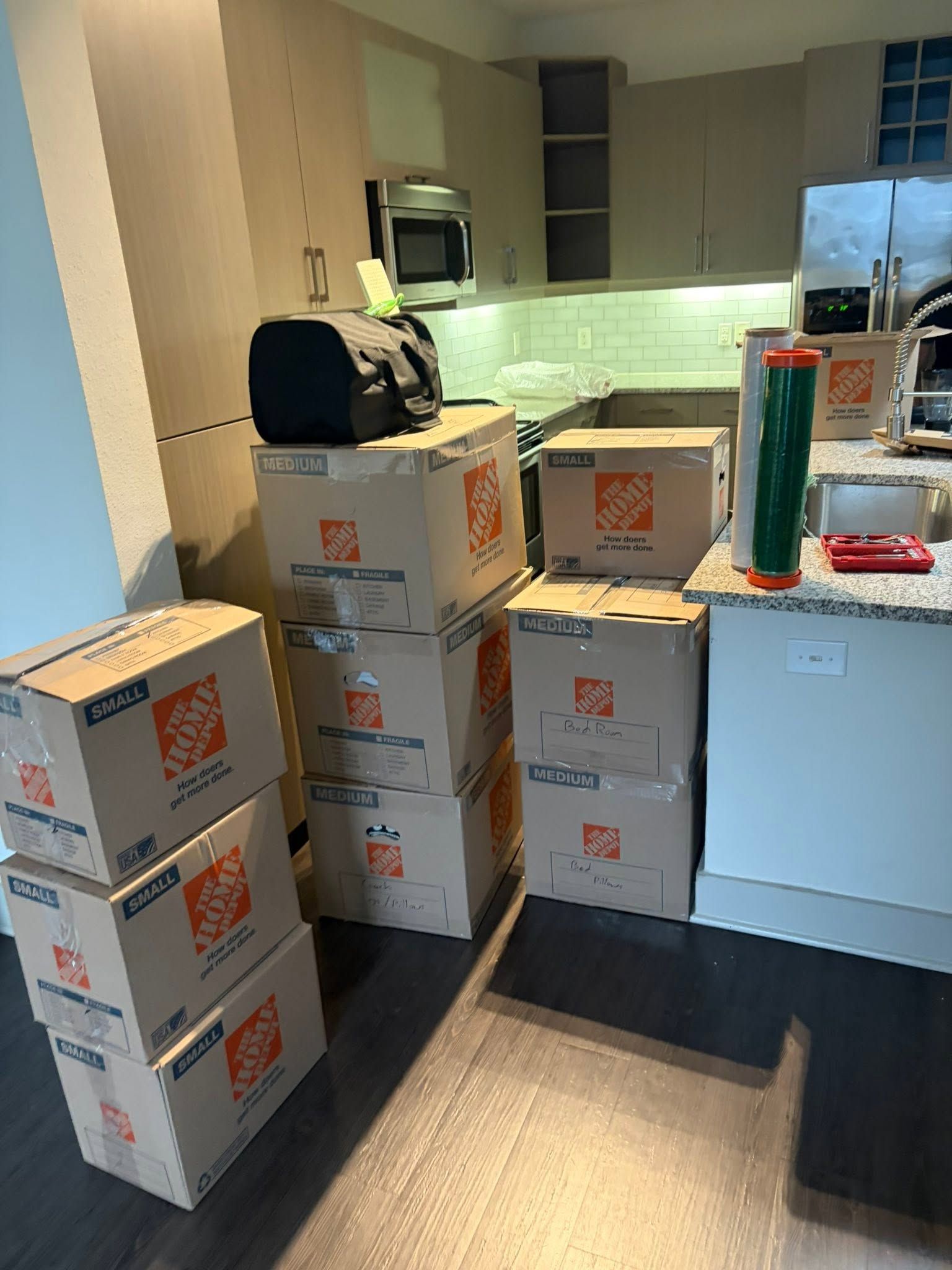 Stacked cardboard boxes in a small kitchen with a white cabinet and countertop appliances.