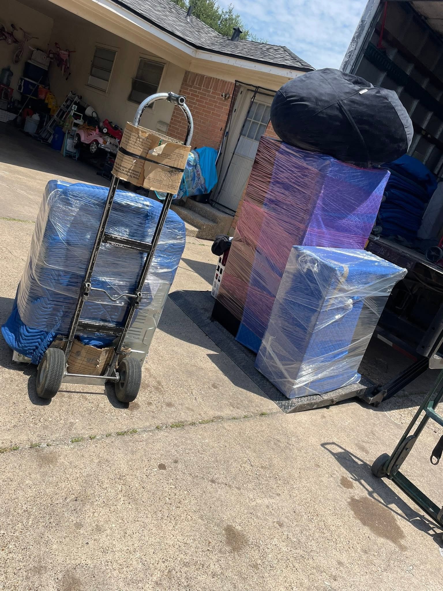Two wrapped carts and furniture items outside a house in bright sunlight.