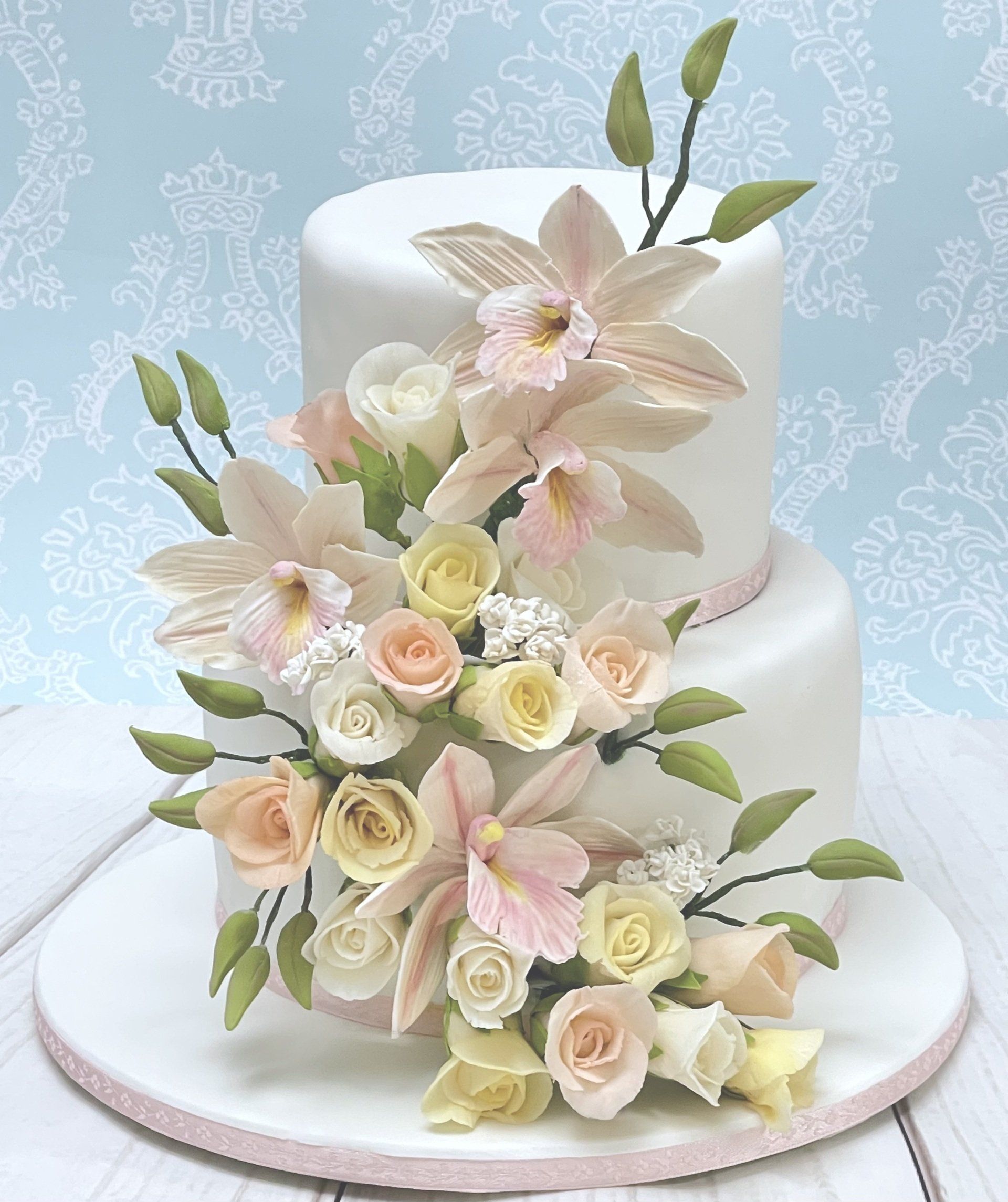 Two tier Wedding cake. White fondant with soft appricot ribbon and a cascade of Sugar cymbidum orchids and small sugar roses in white, soft appricot and soft lemon colours.