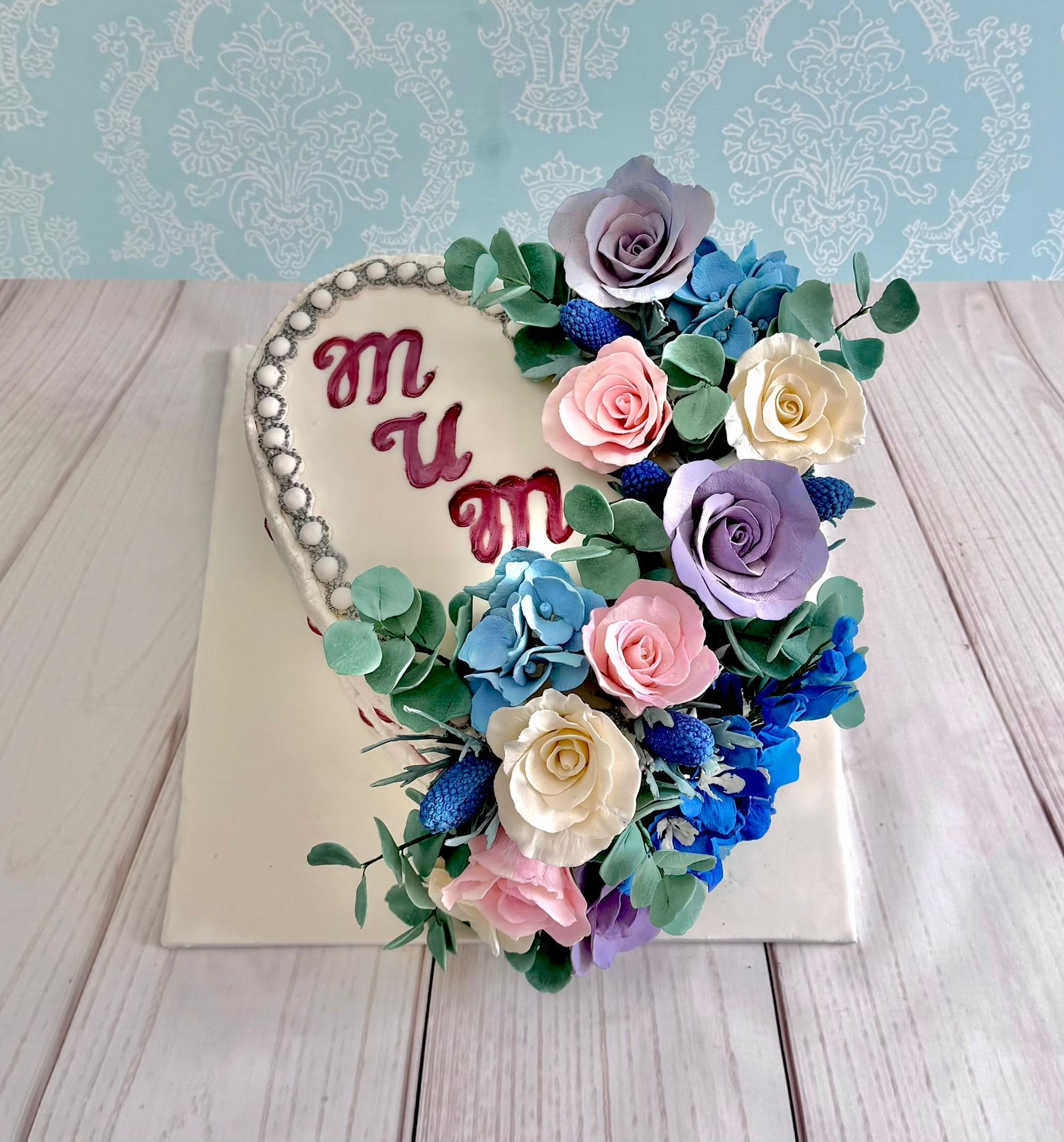 Heart Shaped Cake with a Cascade of sugar flowers , fondant pearl trim and Mum hand painted on the top