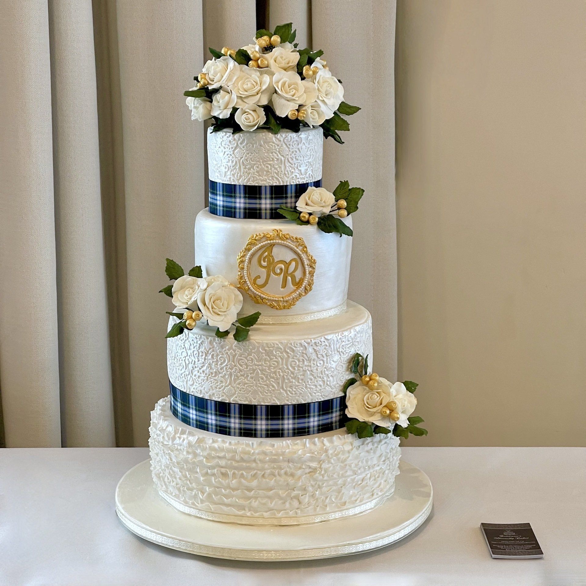 4 tiered wedding cake with pearl white embossed tiers a white ruffle tier the couples tartan, couples initials and lots of sugar flowers.