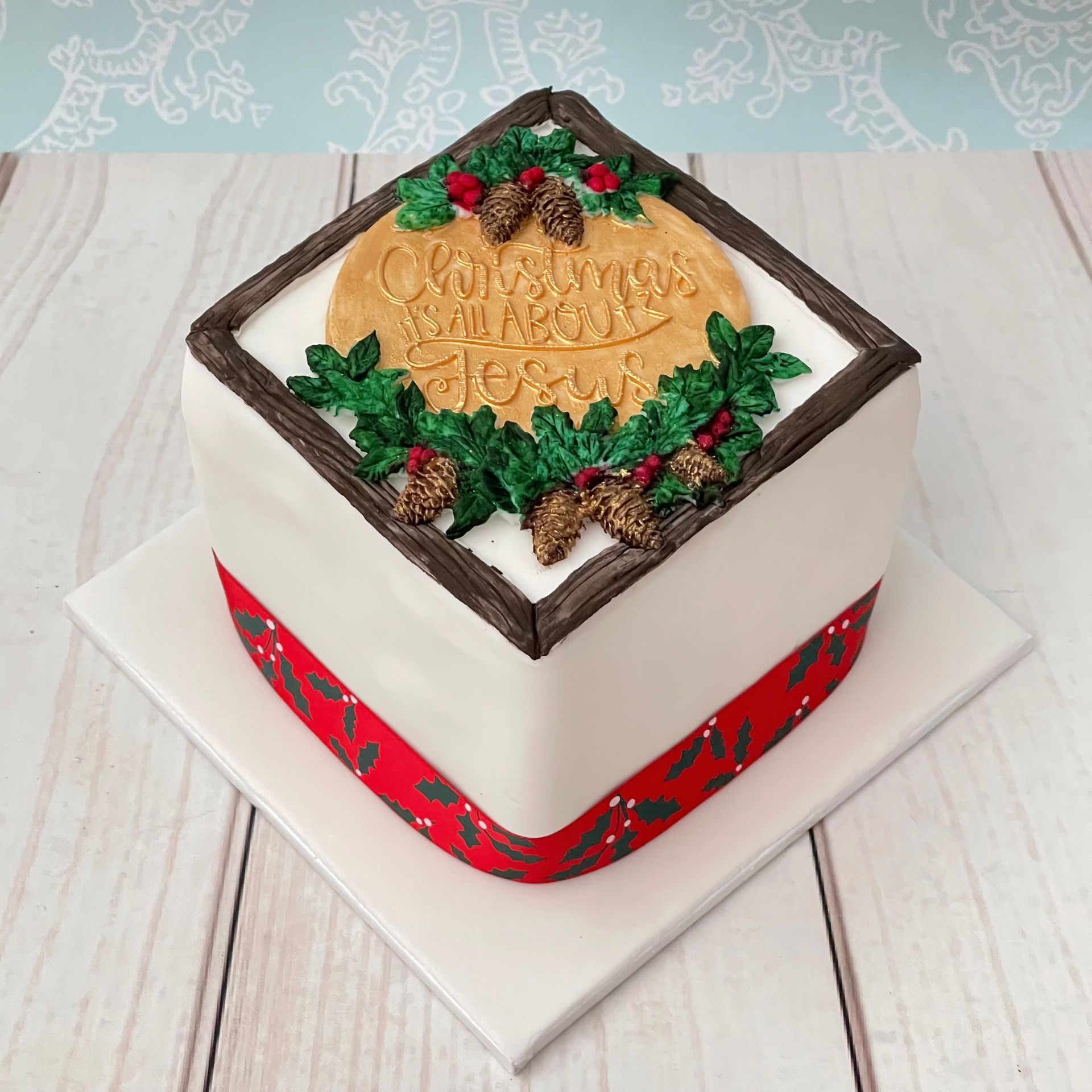 Christmas Cake with fondant wood grain border, holly, and Plaque that says Christmas is all about Jesus