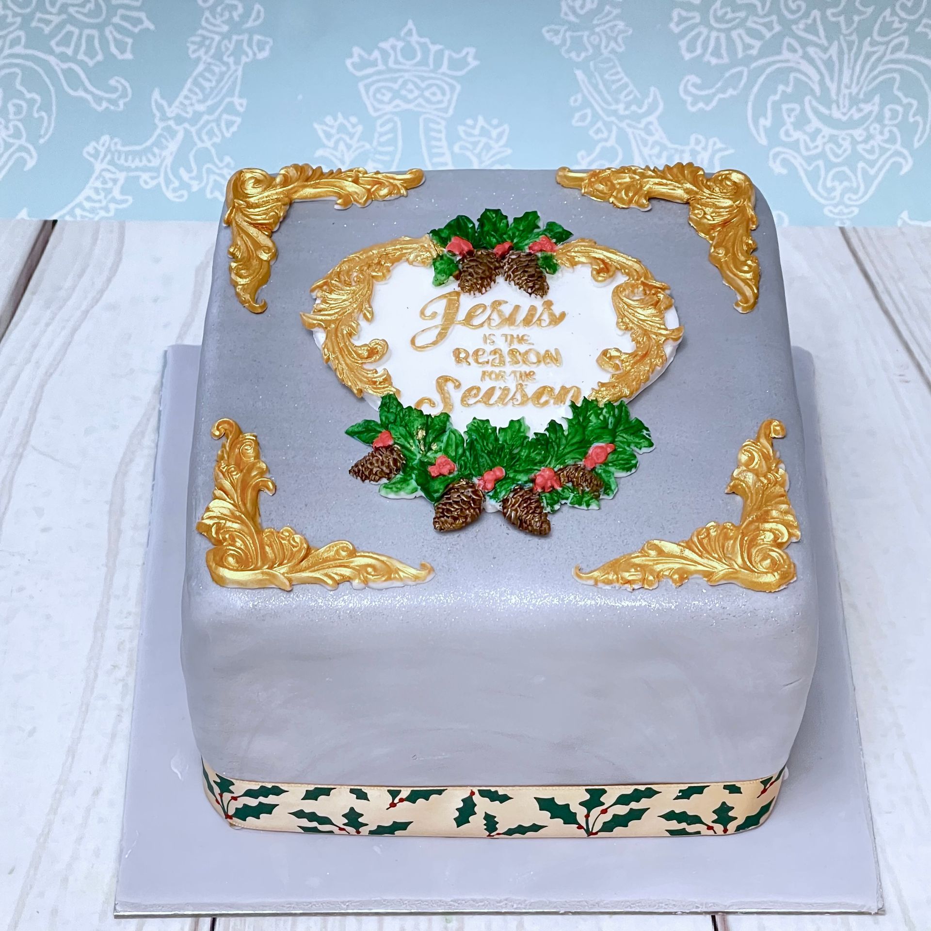 Christmas cake covered in fondant with gold fondant filigree moldings fondant holly fondant pine cones and Hand Painted Jesus is the Reason for the Season fondant heart.