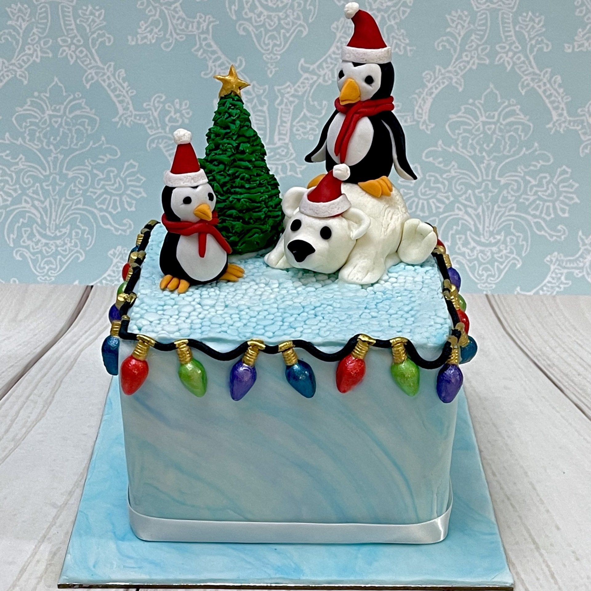 Cute Christmas cake with hand sculpted fondant Christmas Tree, Penguins, Polar Bear and CHristmas Lights.