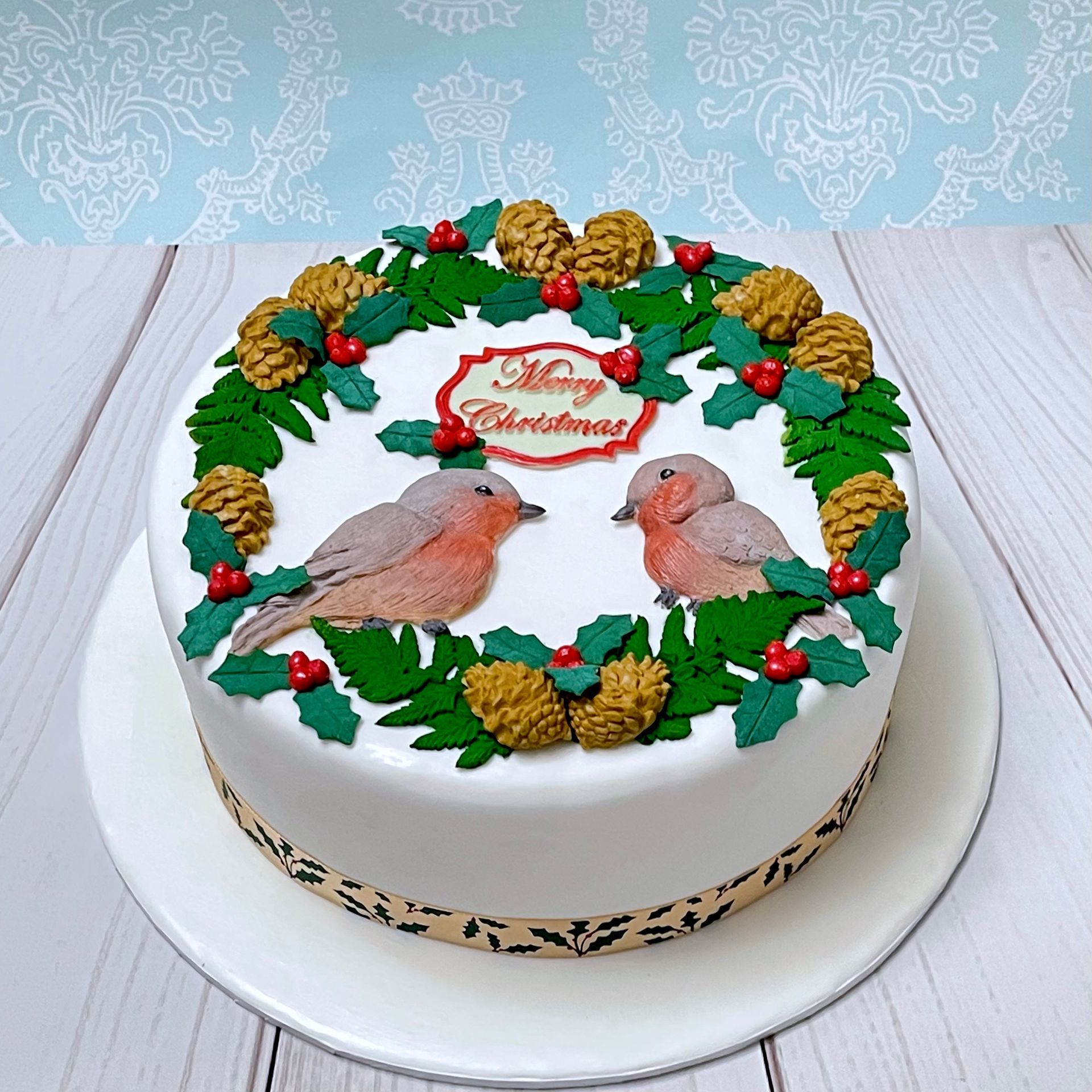 Christmas cake with Christmas Foliage, two fondat Robins, and the words 