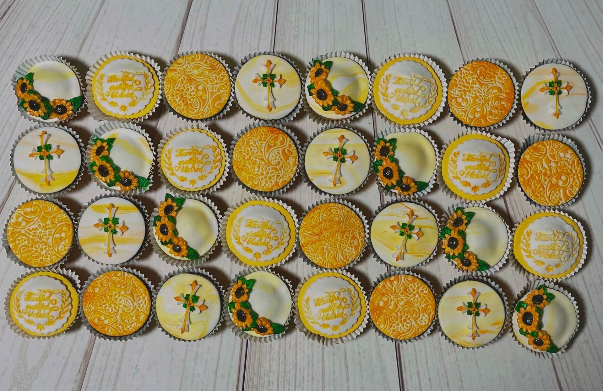 Cupcakes, Some with Sunflowers, Some with Crosses, Some Embossed in yellow and Some with the words 