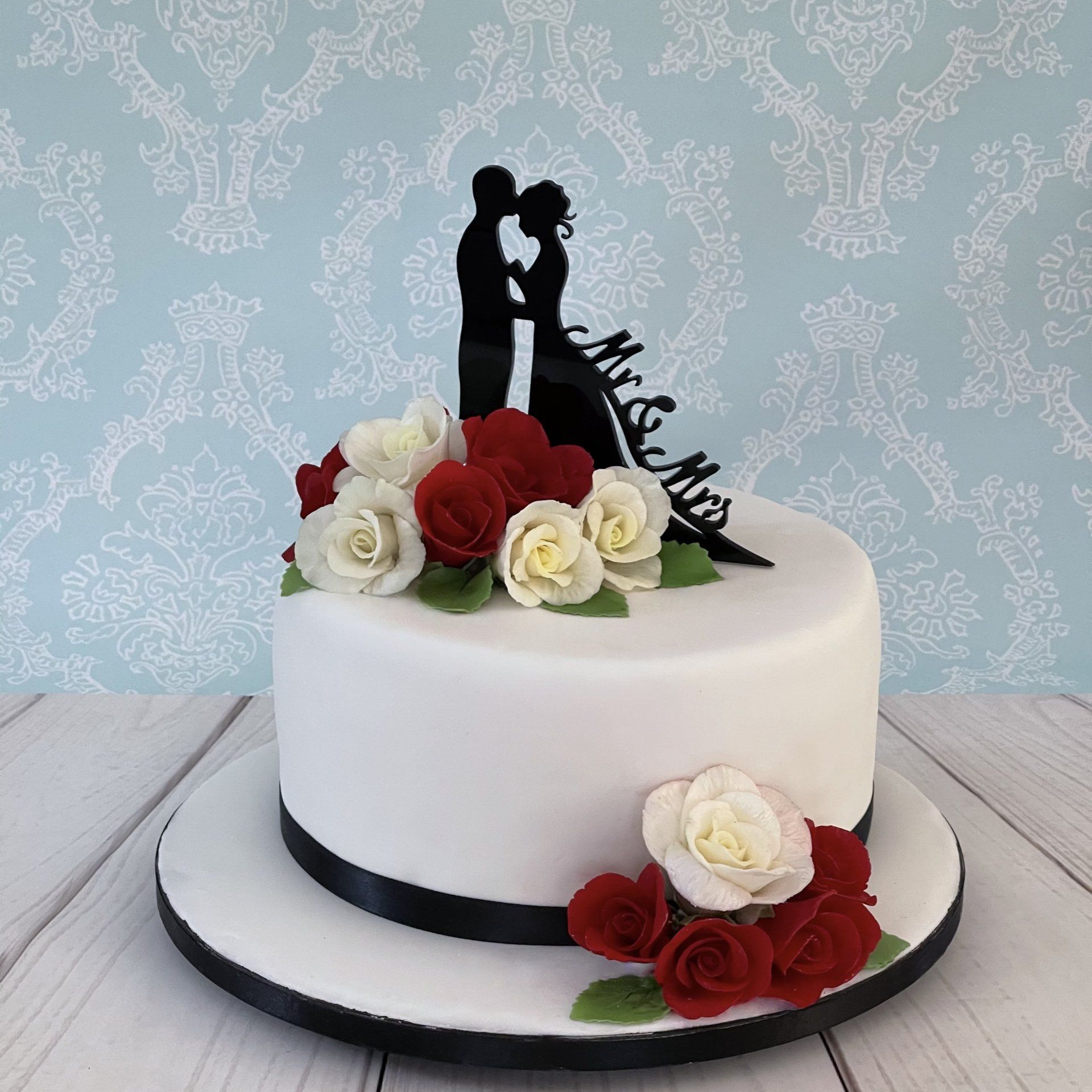 Single Tiered Wedding Cake. White Fondant, Black Ribbon, Red and White Sugar Roses and A Black Silhouette Bride and Groom Topper.