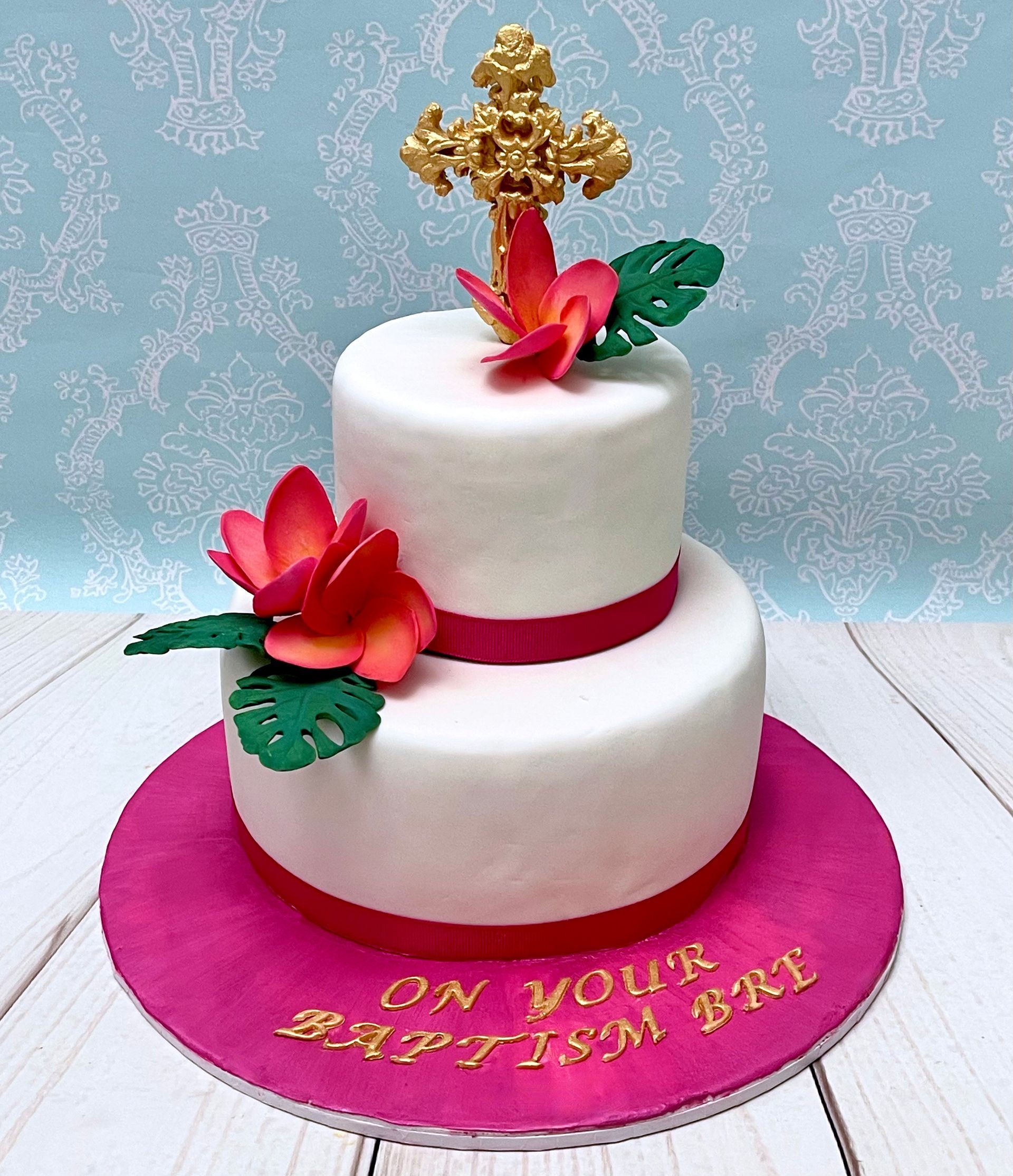 White and hot pink fondant baptism cake with gold fondant cross and handmade pink sugar frangipani flowers
