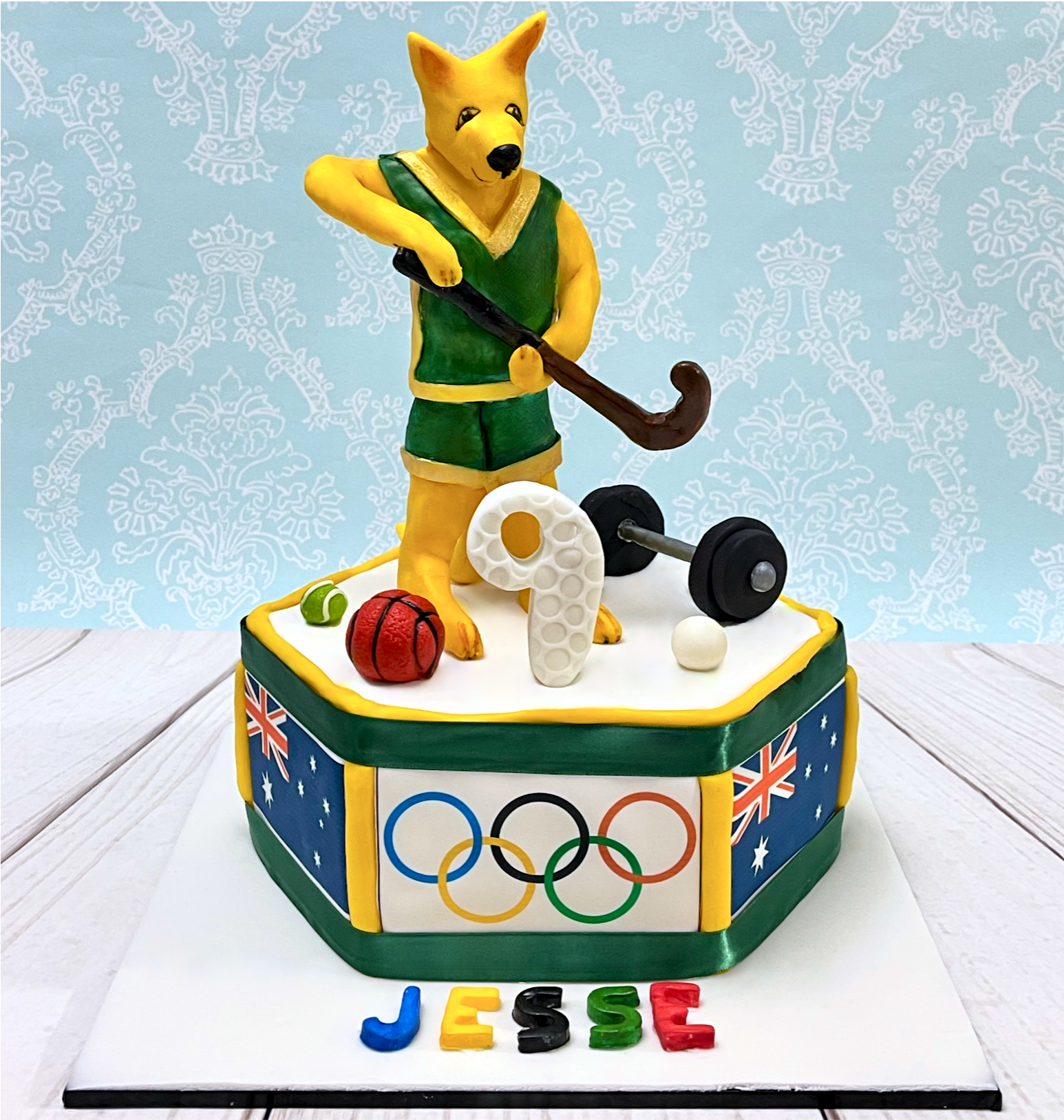9th Birthday Hexagonal Cake with Olympic and Australian Flags around the sides, a Hand-Sculpted Cartoon Kangaroo Playing Hockey, Surround By Other Sport Related Things.