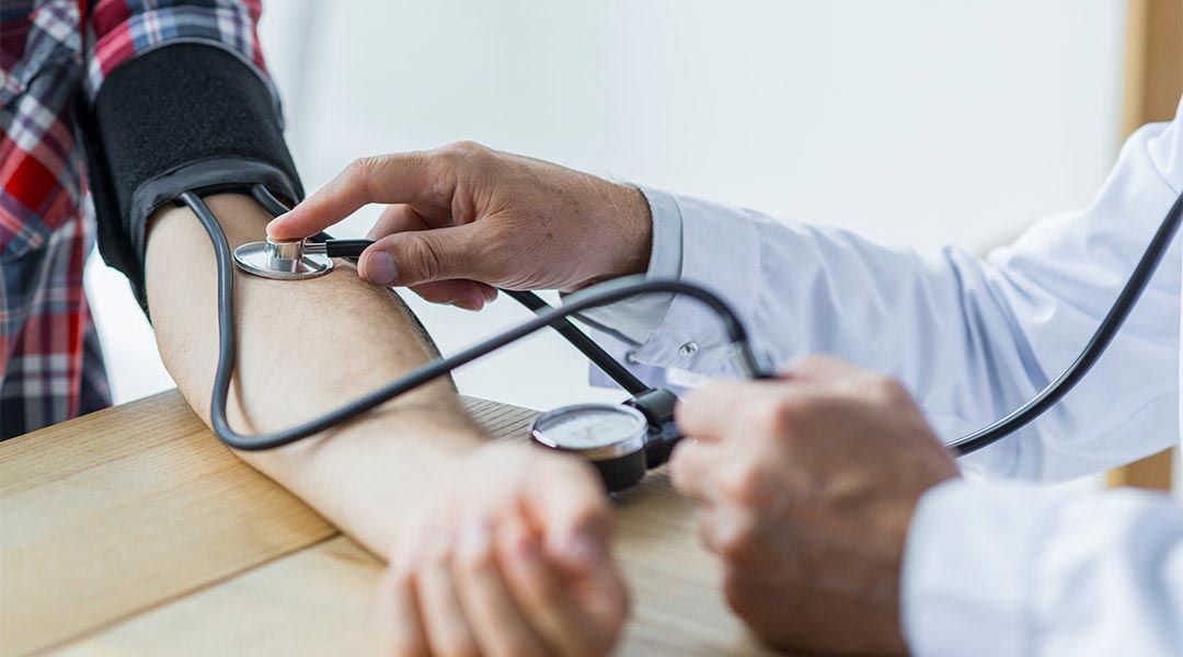 Doctor checking a patient's blood pressure with a cuff and stethoscope on a clinic table