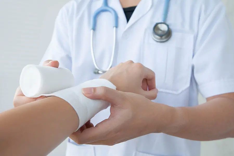 Doctor wrapping a patient’s wrist with a white bandage in a clinic.